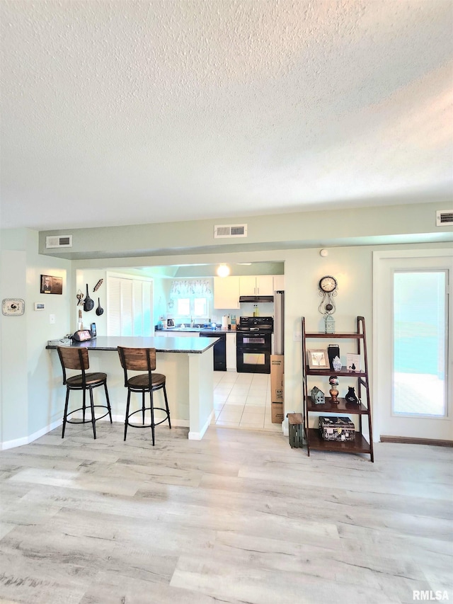 1144 S Morningside Dr, Carbondale, IL 62901 - kitchen with electric range, a kitchen bar, a textured ceiling, light wood-type flooring, and a peninsula