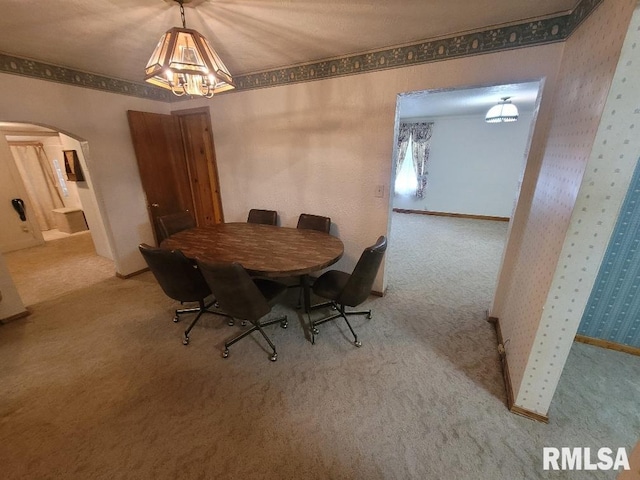 dining space featuring arched walkways, a chandelier, carpet floors, and wallpapered walls