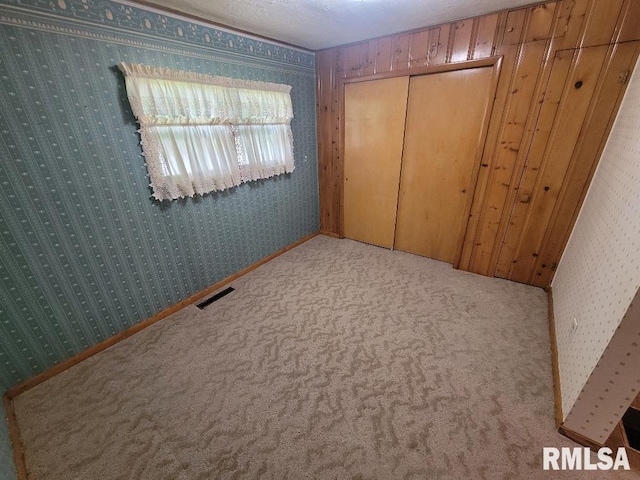 unfurnished bedroom with wallpapered walls, carpet floors, and a closet