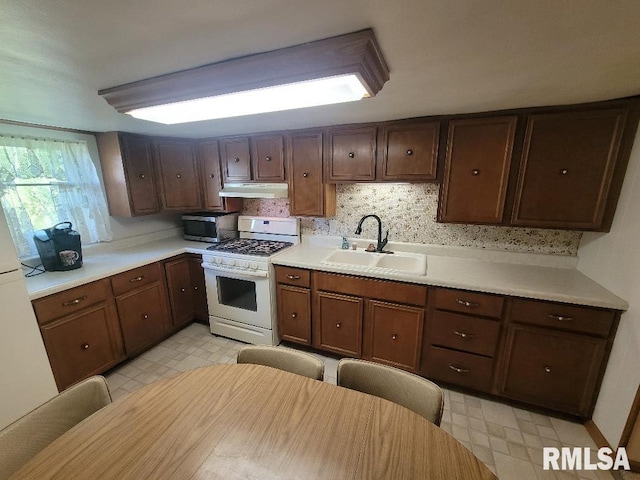 kitchen featuring gas range gas stove, a sink, light flooring, stainless steel microwave, and light countertops