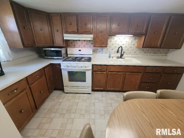 kitchen featuring white gas range, stainless steel microwave, a sink, under cabinet range hood, and light countertops