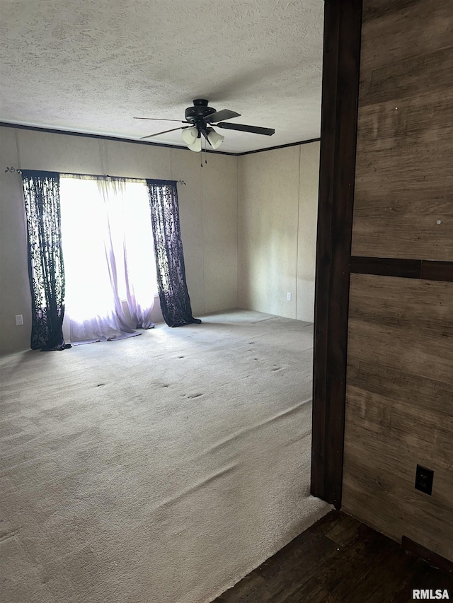 carpeted spare room featuring a textured ceiling, a ceiling fan, and wood walls