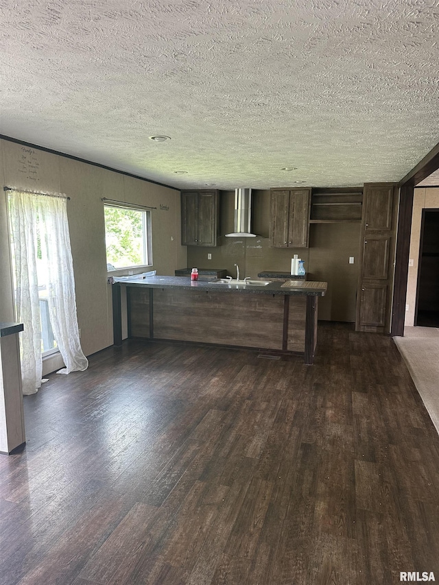 kitchen featuring dark wood-style flooring, wall chimney range hood, and a textured ceiling