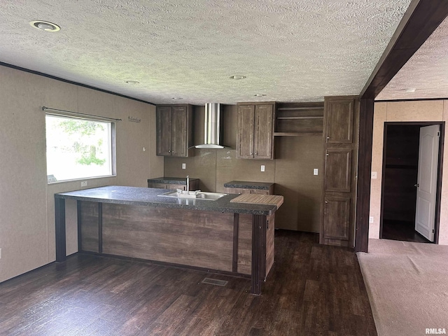kitchen with a sink, wall chimney exhaust hood, a textured ceiling, dark wood-style flooring, and dark brown cabinetry