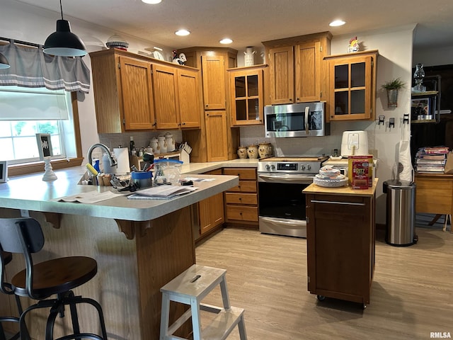 kitchen featuring appliances with stainless steel finishes, a peninsula, brown cabinets, tasteful backsplash, and recessed lighting