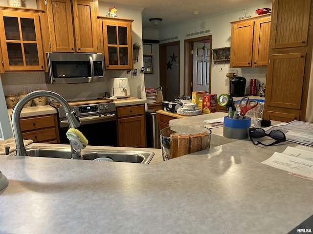 kitchen featuring appliances with stainless steel finishes, a sink, brown cabinets, and glass insert cabinets