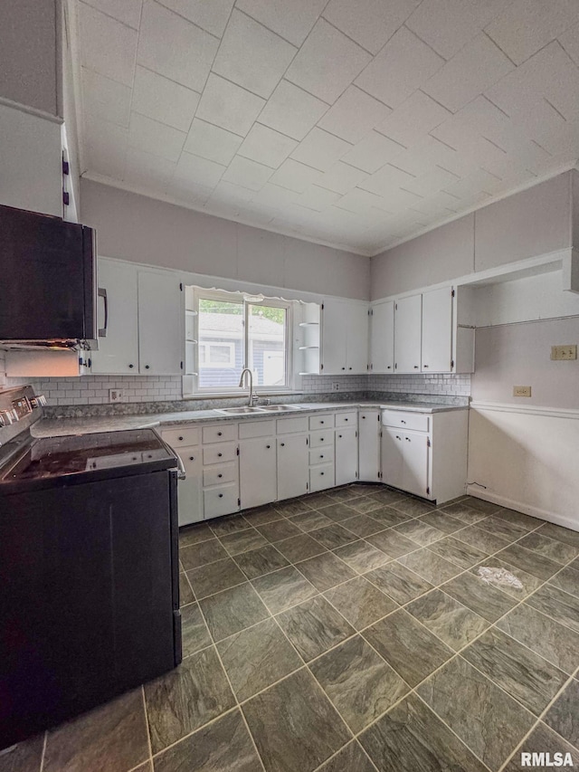 kitchen featuring electric range, a sink, tasteful backsplash, white cabinets, and dark stone finish floors