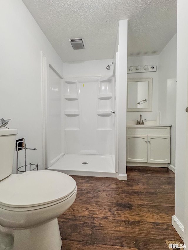 full bath with toilet, wood finished floors, a shower stall, a textured ceiling, and vanity