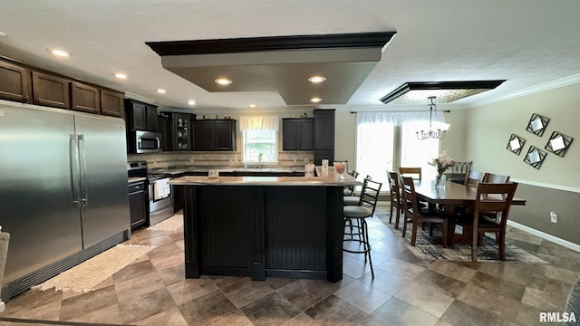 kitchen with stainless steel appliances, ornamental molding, tasteful backsplash, light countertops, and a breakfast bar area