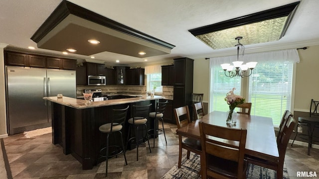 kitchen featuring stainless steel appliances, a chandelier, backsplash, ornamental molding, and a kitchen island