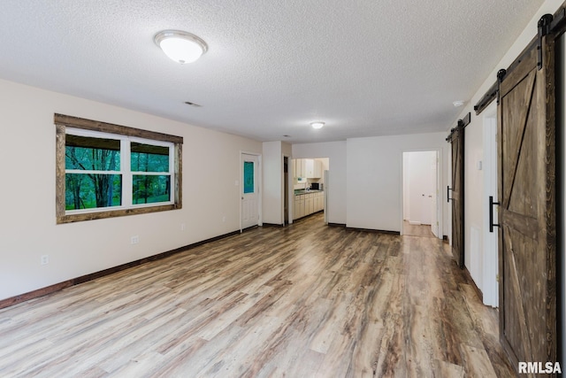 880 State Route 166, Creal Springs, IL 62922 - unfurnished living room featuring a barn door, light wood finished floors, and a textured ceiling