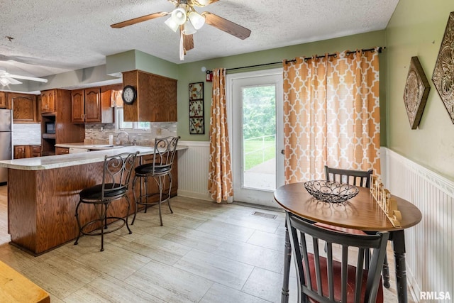 16777 Dublin St, West Frankfort, IL 62896 - kitchen featuring ceiling fan, a textured ceiling, freestanding refrigerator, a peninsula, and a wainscoted wall