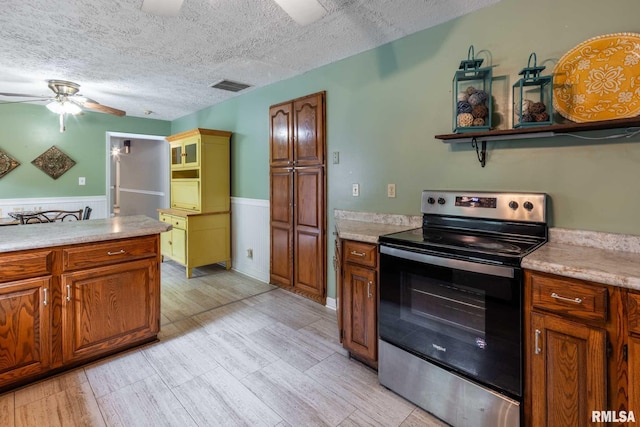 16777 Dublin St, West Frankfort, IL 62896 - kitchen with stainless steel electric stove, a ceiling fan, a wainscoted wall, brown cabinets, and a textured ceiling