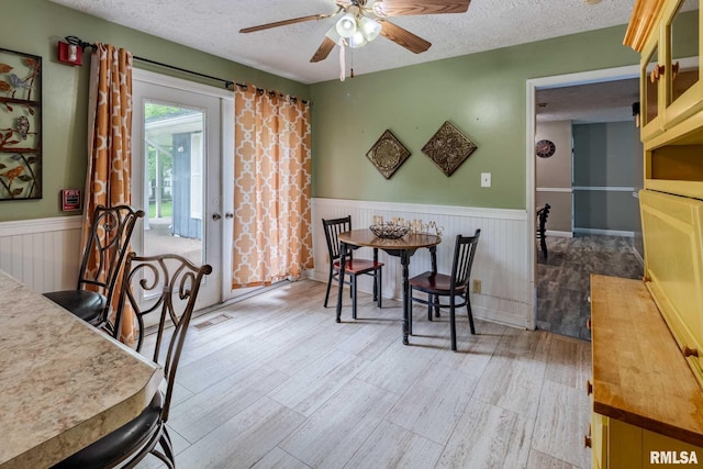 16777 Dublin St, West Frankfort, IL 62896 - dining space with a wainscoted wall, a textured ceiling, a ceiling fan, and light wood-type flooring