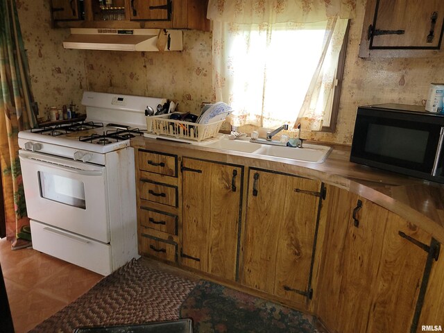 1060 W 5th St, Flora, IL 62839 - kitchen featuring white gas stove, black microwave, range hood, wallpapered walls, and brown cabinetry