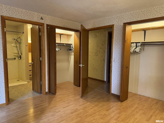 3100 Ava Rd, Murphysboro, IL 62994 - unfurnished bedroom with light wood-type flooring, wallpapered walls, two closets, a textured ceiling, and connected bathroom