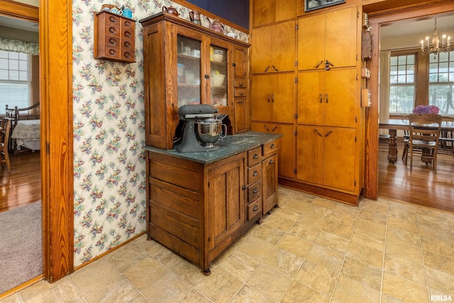 2011 Logan St, Murphysboro, IL 62966 - kitchen featuring brown cabinets, a chandelier, wallpapered walls, dark countertops, and glass insert cabinets