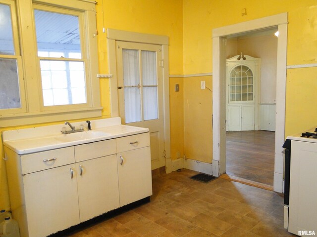 kitchen with white range oven, tile flooring, white cabinetry, and sink