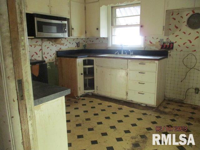 kitchen with dark countertops, beverage cooler, stainless steel microwave, and a sink