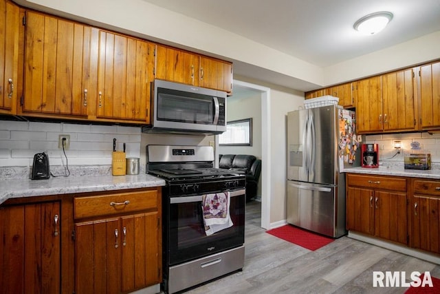 kitchen with backsplash, light stone counters, light wood-type flooring, and appliances with stainless steel finishes