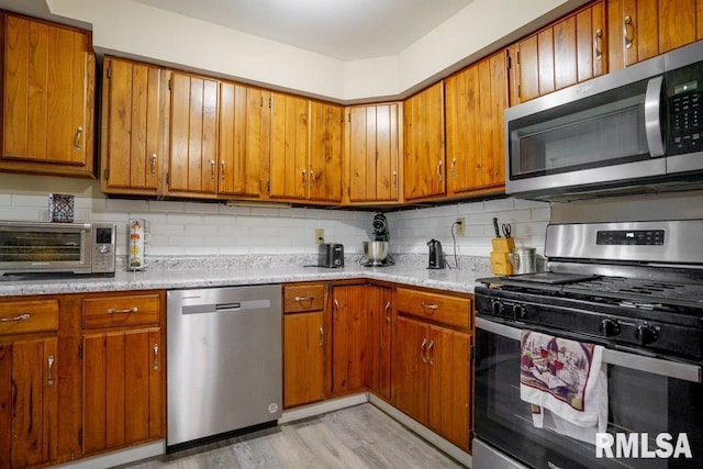 kitchen with light hardwood / wood-style floors, appliances with stainless steel finishes, light stone countertops, and tasteful backsplash