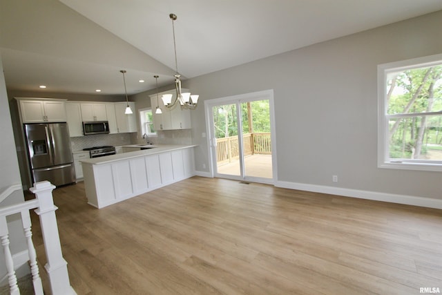 kitchen with appliances with stainless steel finishes, tasteful backsplash, vaulted ceiling, pendant lighting, and white cabinets