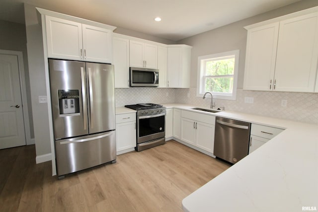 kitchen featuring decorative backsplash, appliances with stainless steel finishes, sink, white cabinets, and light hardwood / wood-style floors