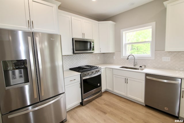 kitchen with appliances with stainless steel finishes, light hardwood / wood-style flooring, white cabinetry, and sink