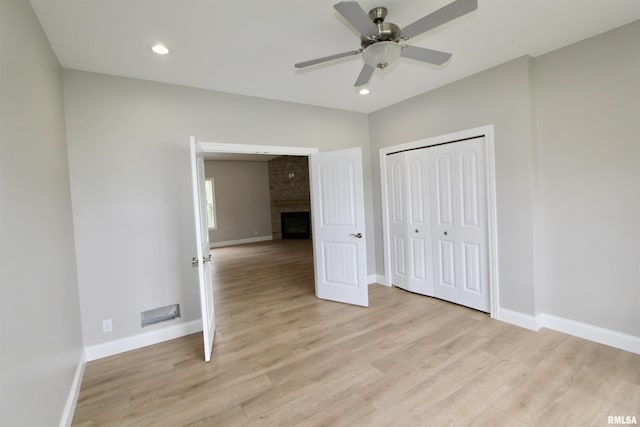 unfurnished bedroom with a fireplace, light wood-type flooring, a closet, and ceiling fan