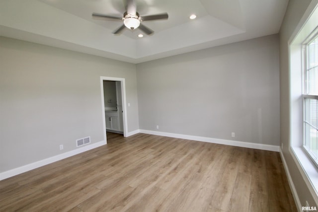 unfurnished room with ceiling fan, light hardwood / wood-style flooring, and a tray ceiling