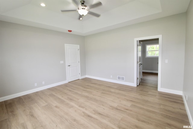 empty room featuring a raised ceiling, ceiling fan, and light hardwood / wood-style floors