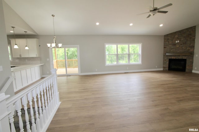 unfurnished living room featuring ceiling fan with notable chandelier, light hardwood / wood-style flooring, a stone fireplace, and lofted ceiling