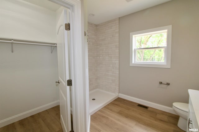 bathroom featuring toilet, wood-type flooring, and tiled shower