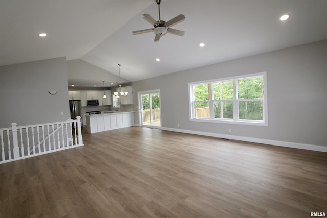 unfurnished living room with ceiling fan with notable chandelier, vaulted ceiling, and hardwood / wood-style flooring