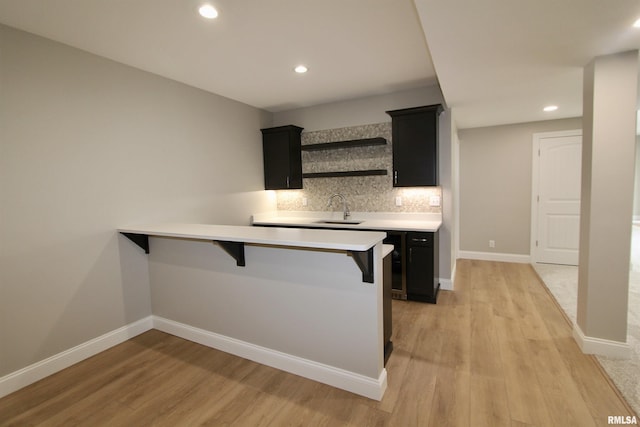 kitchen with kitchen peninsula, a kitchen breakfast bar, tasteful backsplash, sink, and light hardwood / wood-style flooring