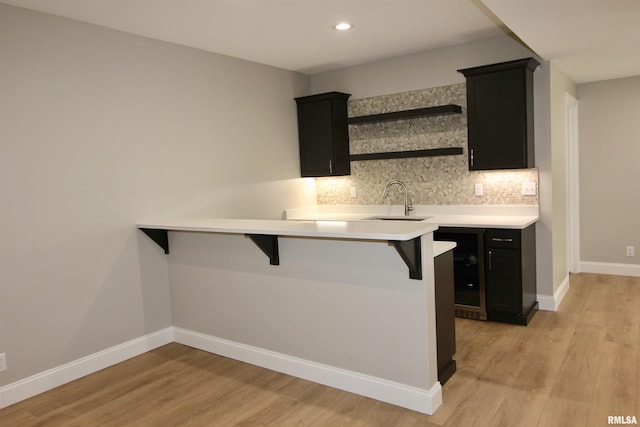 bar with tasteful backsplash, light hardwood / wood-style floors, and sink