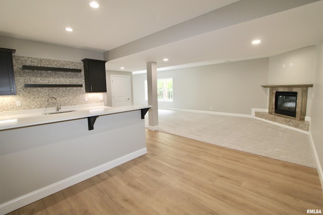 kitchen with a tile fireplace, sink, tasteful backsplash, a breakfast bar area, and light wood-type flooring