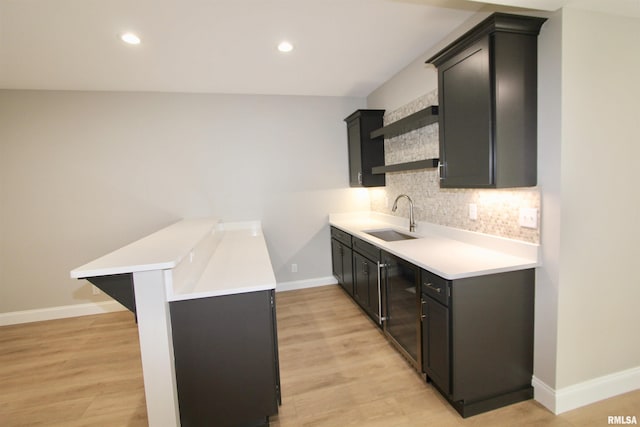 kitchen featuring kitchen peninsula, backsplash, a breakfast bar, sink, and light hardwood / wood-style flooring