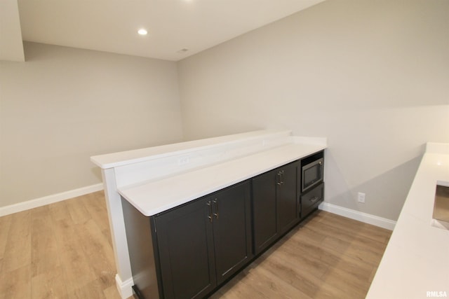 bar with light hardwood / wood-style floors and stainless steel microwave