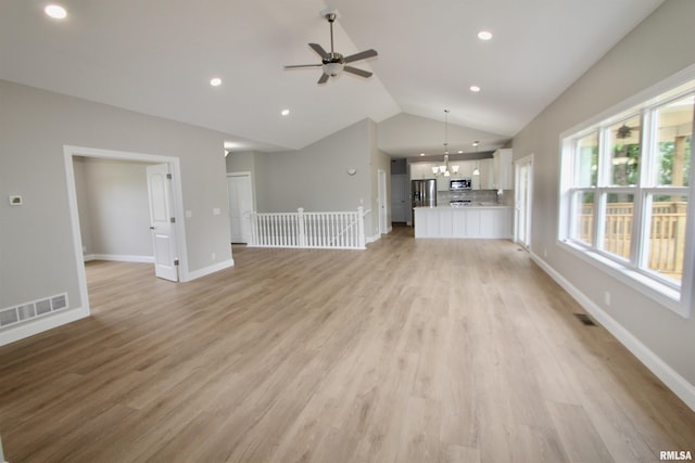 unfurnished living room with ceiling fan with notable chandelier, vaulted ceiling, and light wood-type flooring