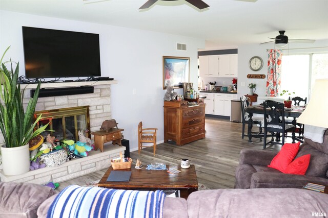 living room with wood-type flooring, ceiling fan, and a stone fireplace