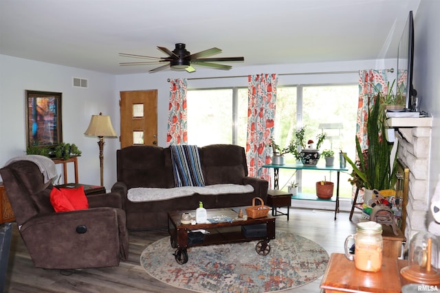 living room with a stone fireplace, ceiling fan, and hardwood / wood-style flooring