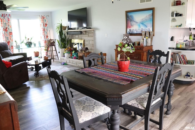 dining room with a stone fireplace, ceiling fan, and hardwood / wood-style floors