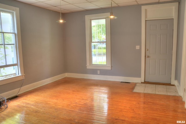 spare room featuring a drop ceiling, light wood-style flooring, and baseboards