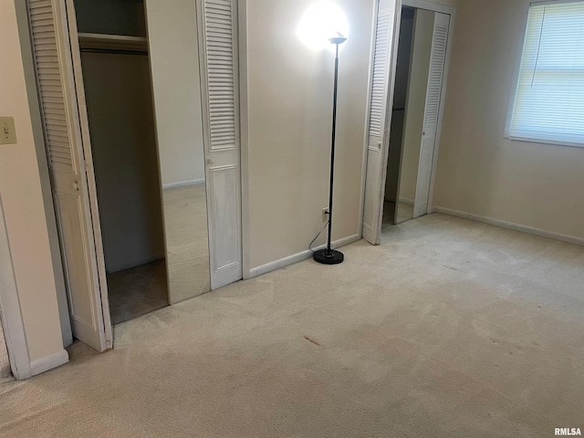 unfurnished bedroom with light colored carpet and multiple closets