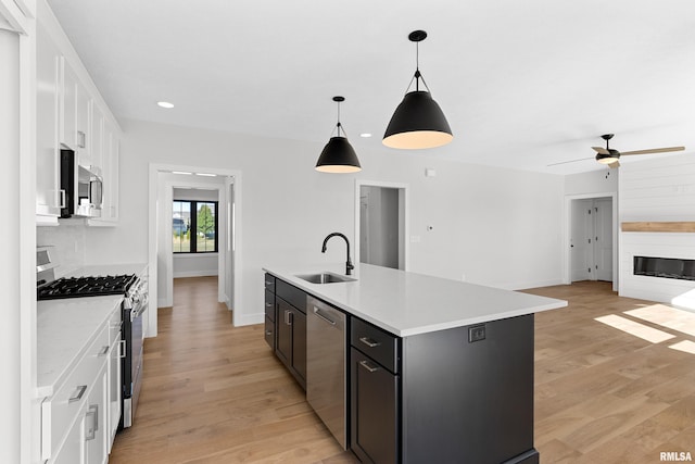 kitchen with sink, white cabinetry, stainless steel appliances, pendant lighting, and a center island with sink