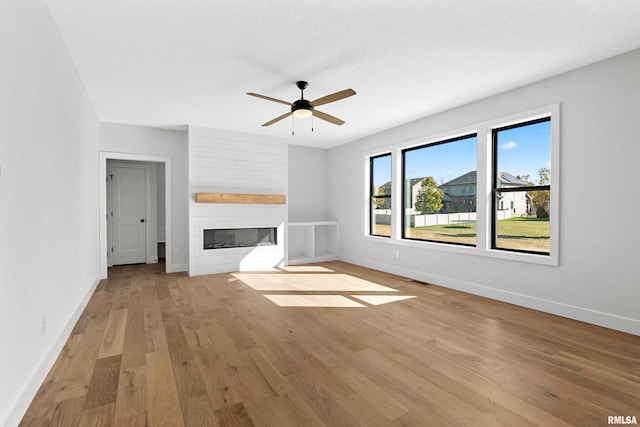 unfurnished living room with light hardwood / wood-style flooring, a large fireplace, and ceiling fan