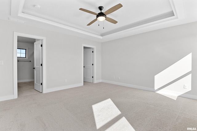 unfurnished bedroom with light carpet, a tray ceiling, and ceiling fan