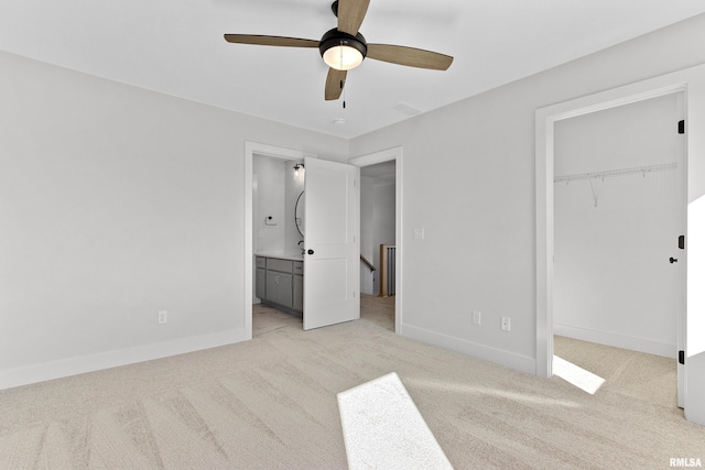 unfurnished bedroom featuring ceiling fan, ensuite bath, a walk in closet, and light colored carpet