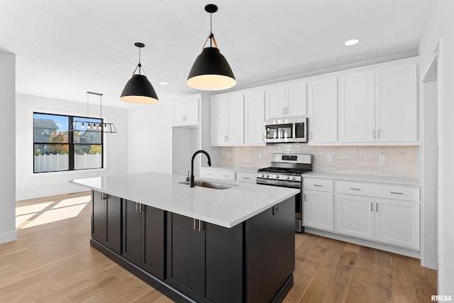 kitchen featuring a center island with sink, white cabinetry, stainless steel appliances, decorative light fixtures, and sink